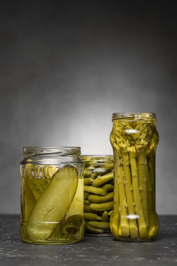 vista frontal de frascos de vidrio con pepinos encurtidos y esparragos